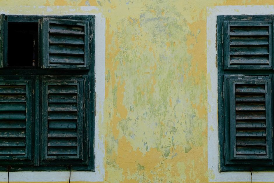 Close-up of rustic wooden louvered shutters on a faded yellow wall, exuding a vintage charm.
