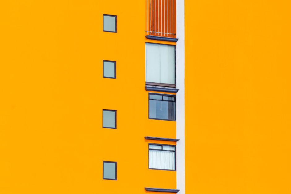 Facade of residential house with bright orange wall with small glass glass windows in daylight in street in city outside