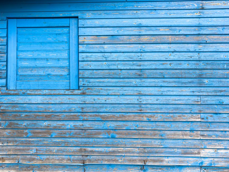 Close-up of a weathered blue wooden building wall with peeling paint and natural texture.